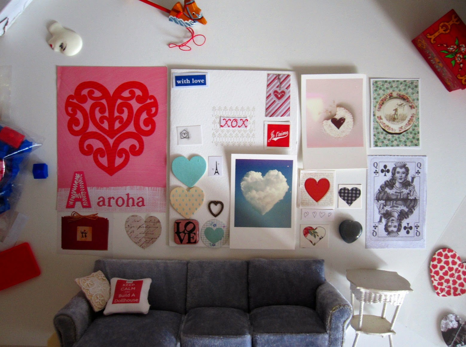 Modern dolls' house miniature grey sectional sofa and cane table with a selection of heart-themed images arranged 'above' them on a wall (actually a desk, with the dolls' house furniture tuned sideways).
