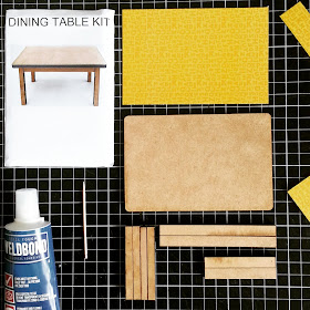 Pieces for a one-twelfth scale dining table kit, including glue, toothpick and patterned paper for the tabletop, all laid out on a cutting mat.