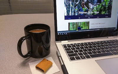 Laptop opened on desk next to a cup of coffee and a fig newton cookie