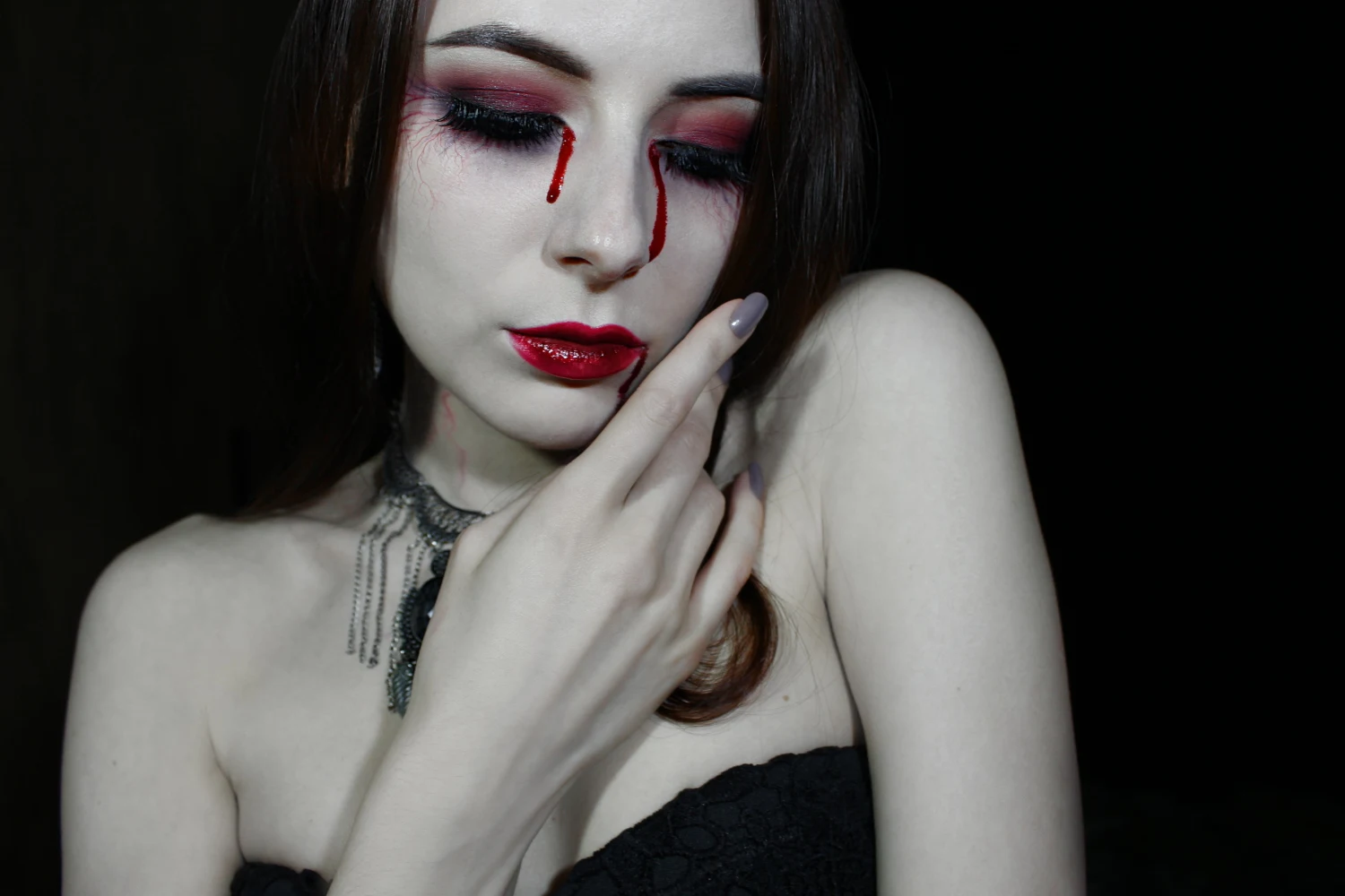 a close-up of pale woman's face with a dramatic vampire makeup look and false blood tears for Halloween.