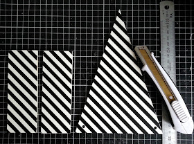 Two rectangular and one bunting-shaped pieces of plywood printed with black and white stripes,laid out on a cutting mat, along with a metal ruler and a utility knife.
