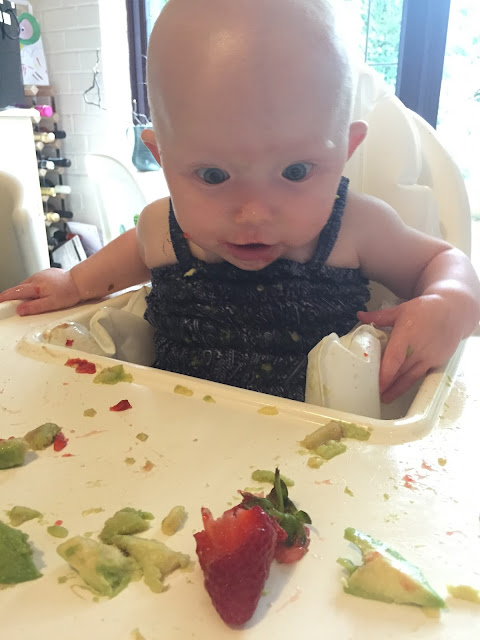 A baby looks in wonder at a partially munched strawberry on her high chair tray