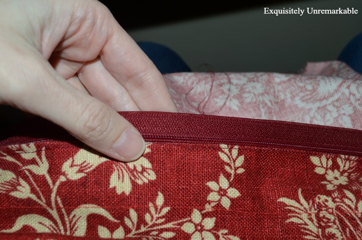 Hand holding zipper in place on red pillow cover