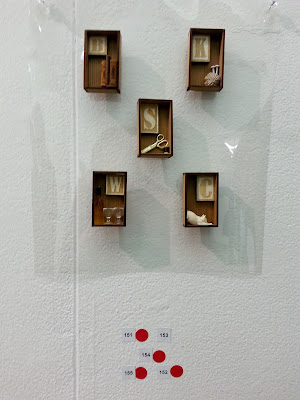 Five miniature brooches on display in a gallery, with four red dots underneath them.