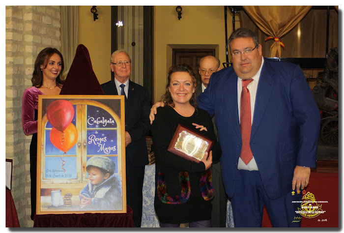 D. Juan Luis Ortíz Seda, le entrega una placa recuerdo a: Dª. Victoria Eugenia García de la Vega Reinoso, autora del Cartel de la Cabalgata del año 2018