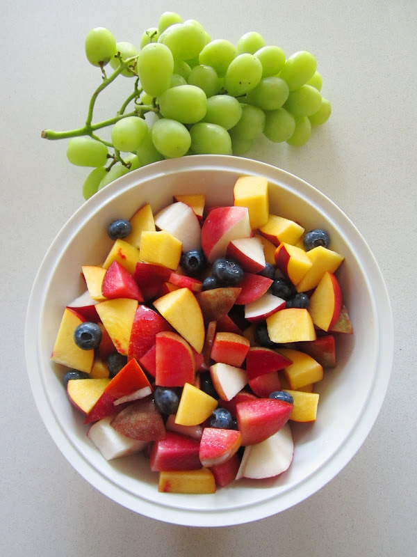 Finish fruit salad in a white bowl with a bunch of green grapes on a white kitchen table