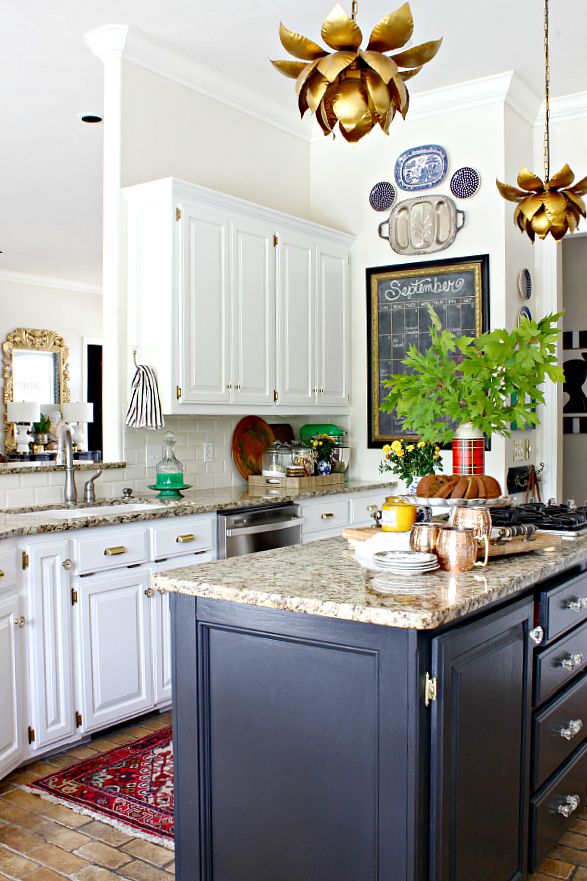 white kitchen cabinets, black island, brass hardware, lotus pendant light, vintage rug