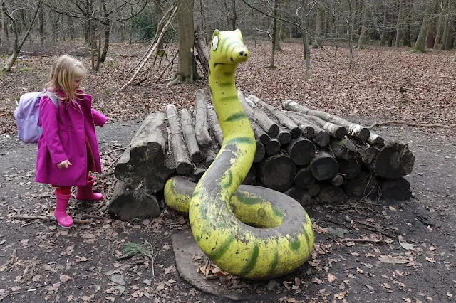 A girl in pink looking at a battered wooden carved large snake