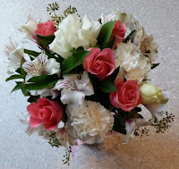 Above-view of a posy of flowers - pink and white roses, white lillies and white carnations with green filling plant (maybe gypsophila).