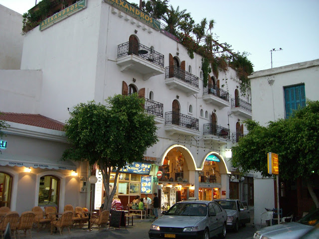 A whiteawashed, square building with eight wrough-iron balconies. The ground floor is a brightly-lit cafe.