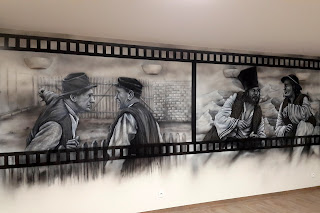 Czarno-białe graffiti Artystyczne malowanie ściany w motyw z filmu "Sami Swoi", czarno-biały mural w sali telewizyjnej