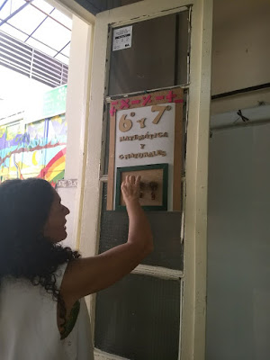 se ve a una maestra pegando carteles de bienvenida en la puerta de un aula
