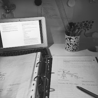 Black and white photo of a desk, with a laptop, pencil pot and lever arch file on it. A method from a chemistry experiment has been copied from the laptop to a piece of paper, which rests on the file.