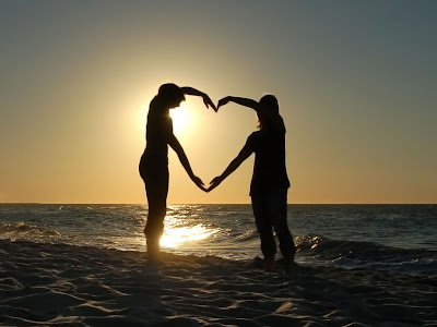 Dos enamorados forman un corazón en la playa