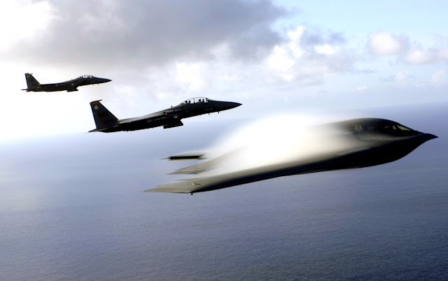 A B-2 Spirit and F-15E Strike Eagles fly in formation across the Pacific Ocean