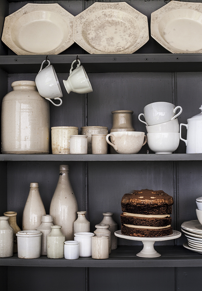 Dark painted shelves in a country cupboard with white stoneware and dishes. Bohemian Chic Home Decor in a White Cottage by Kara Rosenlund. #countrystyle #rusticdecor #vintagedecor #shelves #dishes