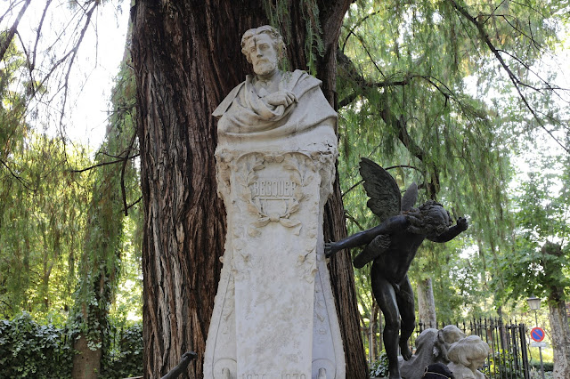Estatua de piedra blanca de Bécquer con un gran árbol y la vegetación de un parque de fondo.