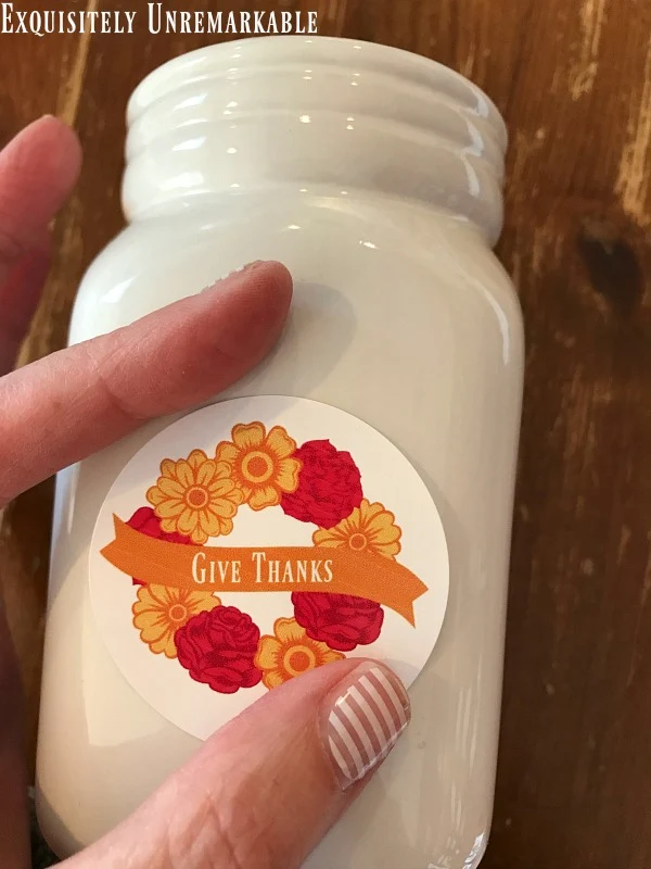 Round give thanks wreath sticker being placed on white mason jar