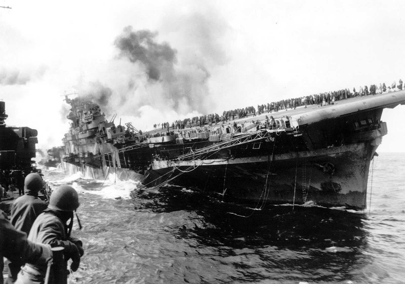 The USS Santa Fe lies alongside the heavily listing USS Franklin to provide assistance after the aircraft carrier had been hit and set afire by a single Japanese dive bomber, during the Okinawa invasion, on March 19, 1945, off the coast of Honshu, Japan. More than 800 aboard were killed, with survivors frantically fighting fires and making enough repairs to save the ship.