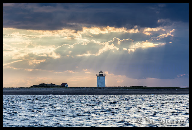 Sunlight shines through clouds onto Long Point Light House On Cape Cod