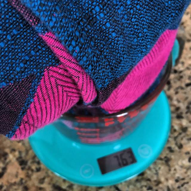 [Image of a pink, blue, and black woven wrap rolled in a large glass Pyrex on top of a teal digital food scale on a kitchen counter. Scale reads 763 grams.]