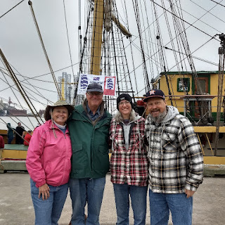 4 people on a dock in front of a tall ship