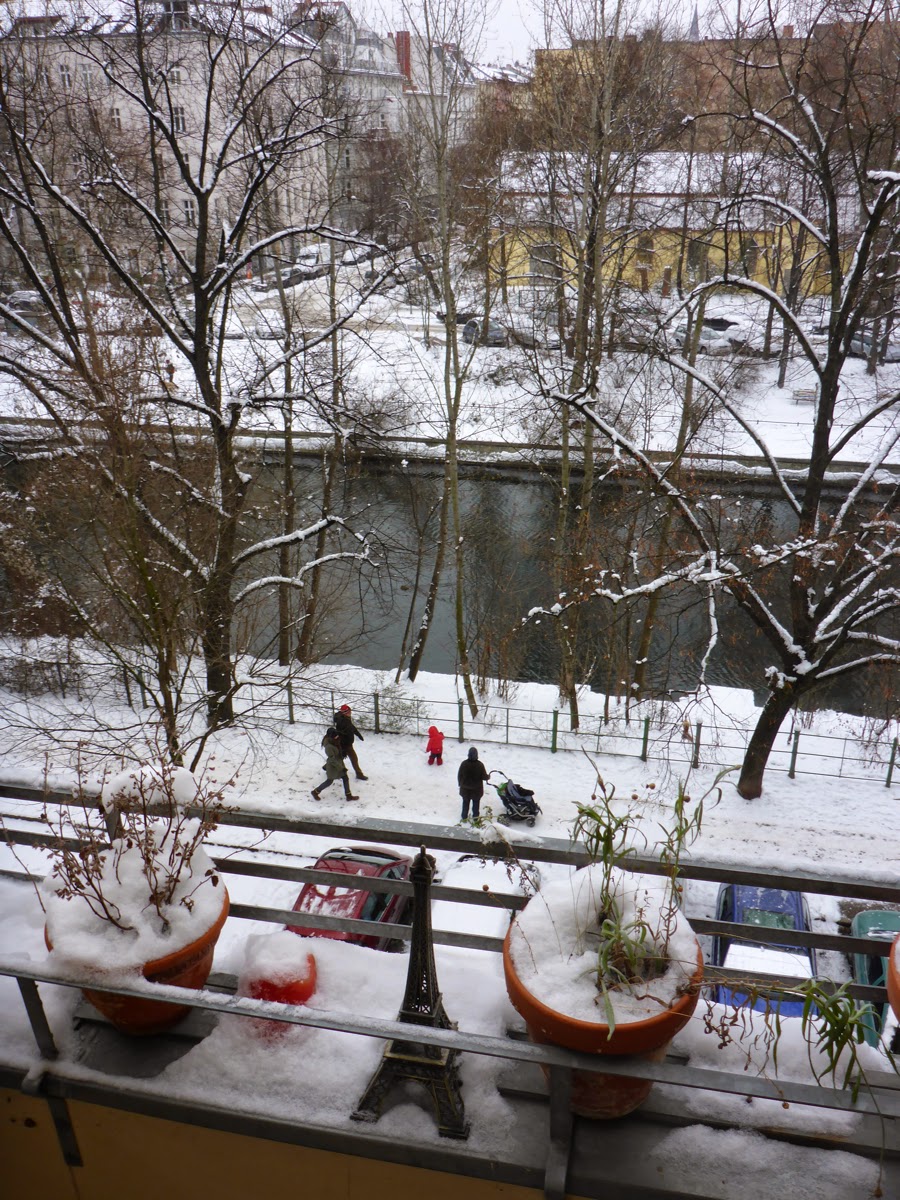 Kanal, Fußgänger, rotgekleidetes Kind, Schnee und Eiffelturmminiatur zwischen den Pflanztöpfen