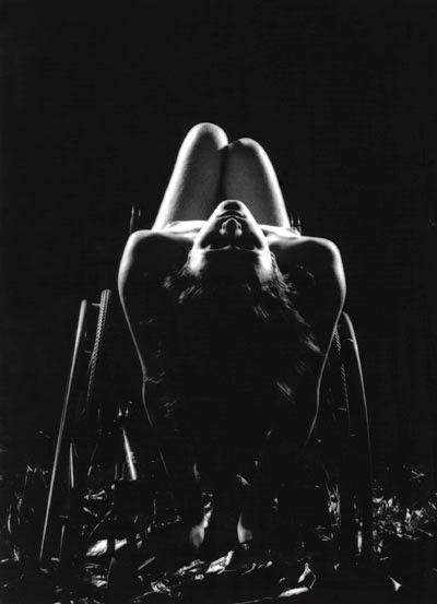 black and white photo of a naked woman leaning back in a manual wheelchair, viewed from the back