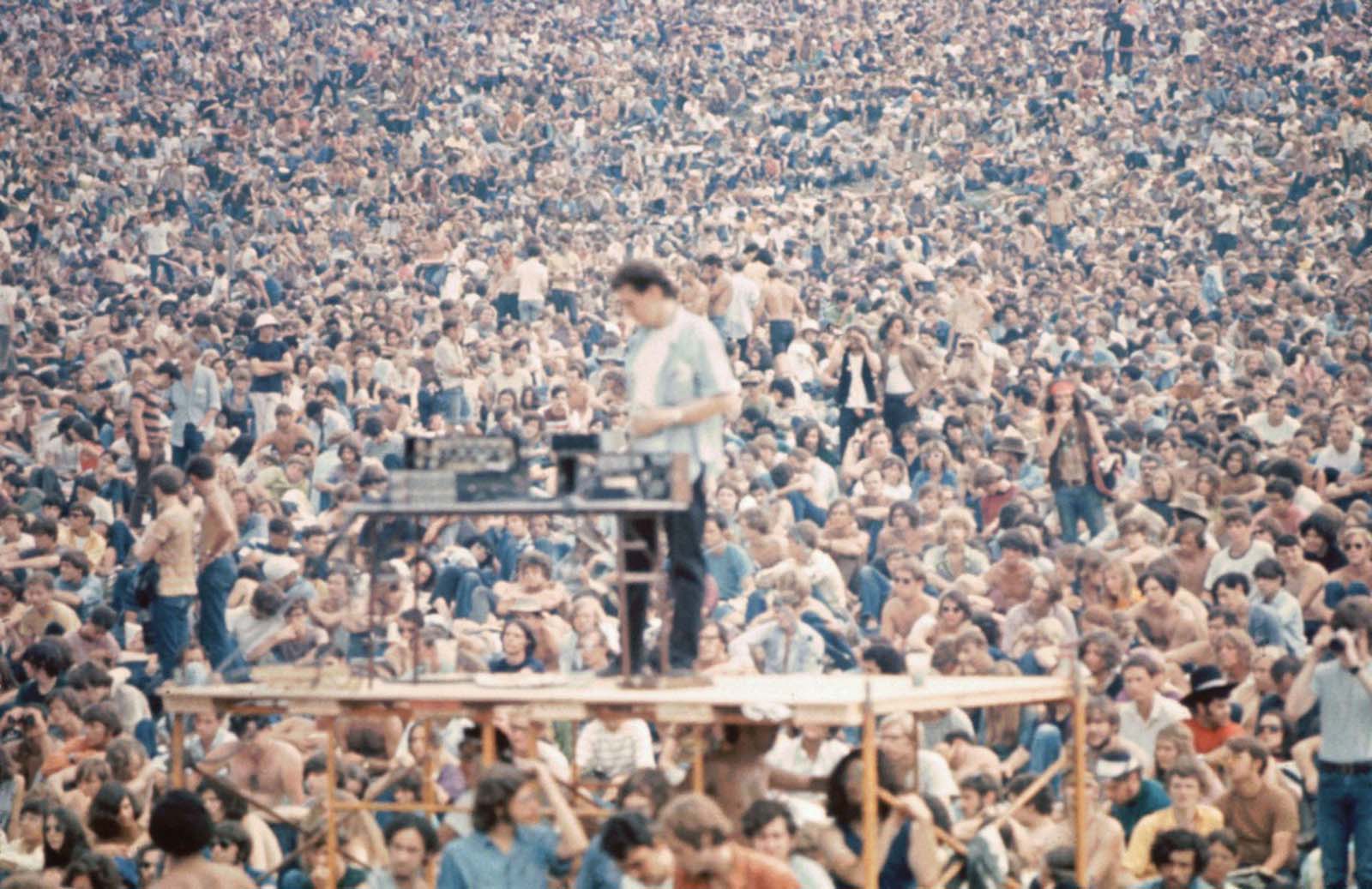 A sound man stands on scaffolding with his equipment in front of the Woodstock crowd.