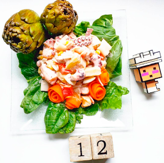ensalada floral dos alcachofas enteras, tiras de zanahoria dando la impresión de ser rosas, ensalada de pulpo en el centro de la imagen rodeado de espinacas