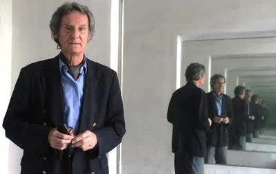 La imagen muestra al poeta Eugenio Mandrini con un saco oscuro sosteniendo unos anteojos, retratado frente a un espejo que lo refleja varias veces