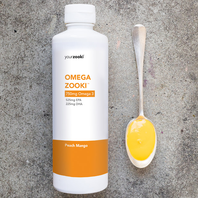 A white bottle of Omega Zooki next to a spoon with an orange liquid in