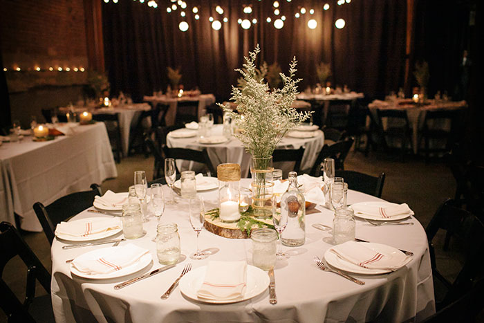 Table decor in their urban-chic wedding reception with cafe lights and greens displayed on cut fir rounds. Photo by Julie Harmsen. table