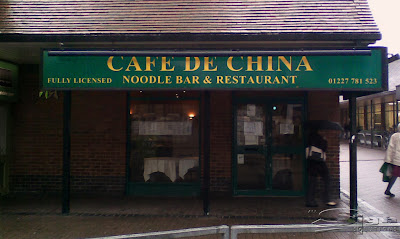 Photograph of green fascia with gold lettering spelling 'Cafe De China' with the telephone number.