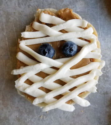 These super simple English muffin mummies are a perfect way to start Halloween. Just a couple of minutes and a few ingredients is all it takes to get the day off on an undead foot! close up of peanut butter and cream cheese mummy face
