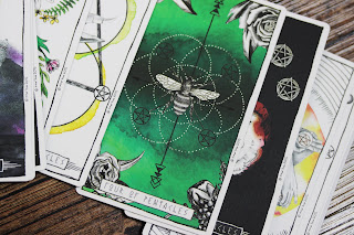 A photo of tarot cards spread out across a wooden surface, with the four of pentacles on top - a dark green card, with a wasp in the center, surrounded by interlinking circles made from white polka dots, and four black pentacles