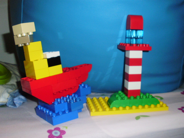 MOC com peças LEGO Duplo, representando um pequeno barco a passar junto a um farol de costa