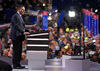 Man in suit standing at podium in crowded auditorium, speaking.
