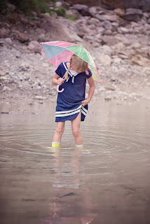 Kind mit Schirm und Gummistiefeln in Pfütze