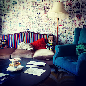 Retro living room with vintage sofa draped with a crocheted rug, and green wing chair with floor lamp behind it.