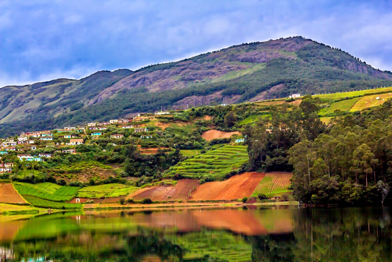 Landscape photo near Avalanche lake Ooty with a mountain in the background and houses on the slope. Lake in the foreground.