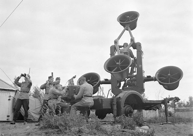 Looking out toward approaching aircraft with binoculars and listening with a huge acoustic locator.