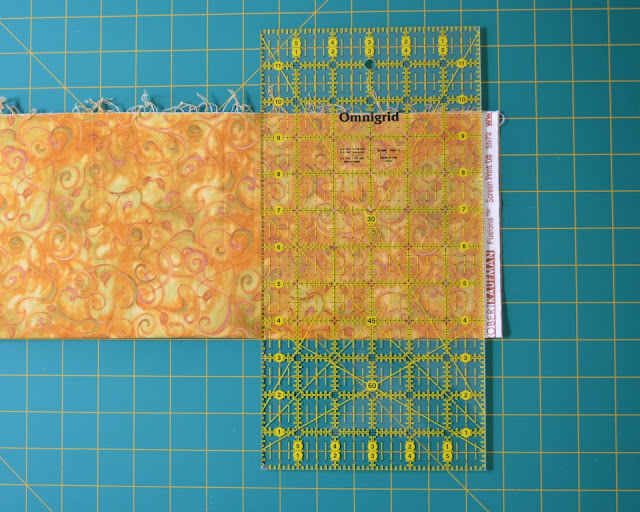 Fabric laid out on cutting mat. A quilter's rule is laid out on top, lined up with the mat grid, ready to trim off the selvage