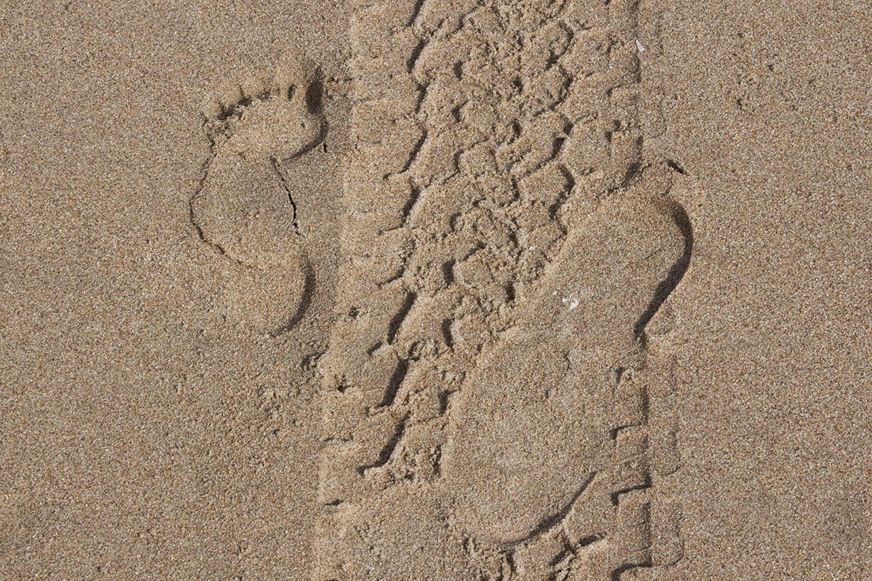 two footsteps and tyre track in sand