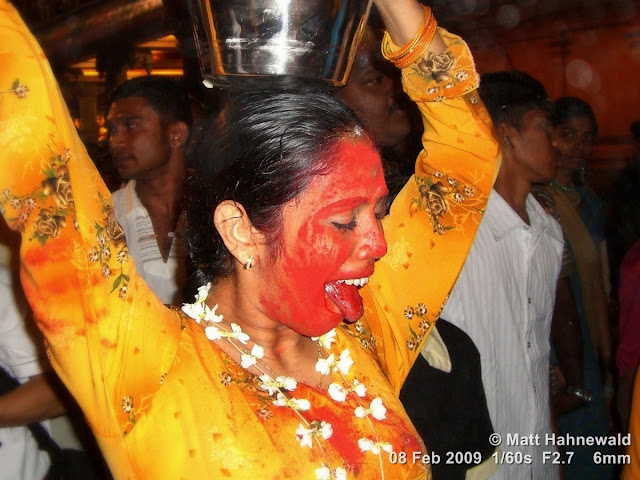 Street portrait of an agitated Malaysian Indian woman with red dye all over her face carrying a ceremonial milk offering during the 2009 Thaipusam Festival at Batu Caves. Thaipusam Festival, Malaysia, Kuala Lumpur, Batu Caves, kavadi attam, ceremonial sacrifice, ceremonial offering, Tamil woman, Hindu woman, Malaysian Indian woman, street portrait, trance