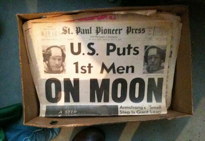 Photo of a box holding a copy of the St Paul Pioneer Press from July 1969 with huge headline U.S. Puts 1st Men ON MOON