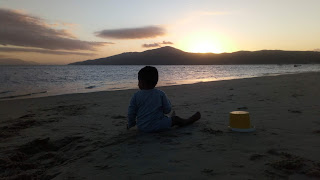 Niño jugando con baldecito y arena en la playa de Mariscal, puesta de sol tras el morro