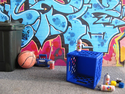 Modern dolls' house miniature street scene of a wall of street art with a milk crate and spray cans in front of it.