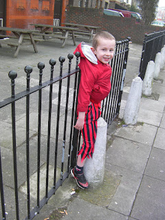 boy hanging off fence by coat