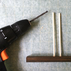 Electric drill laid next to a length of wood with two dowels sticking out of the top of it.